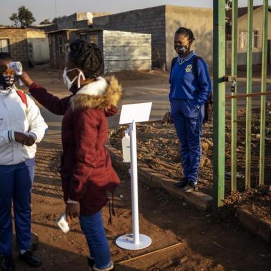 A pupil at the Winnie Mandela Secondary School looks at a teacher taking the temperature of another pupil as she waits in line outside the school premises before classes resume in the Tembisa township, Ekurhuleni, on June 8, 2020. - Grade 7 and grade 12 pupils in South Africa began returning to classrooms on June 8, 2020  after two and a half months of home-schooling to limit the spread of the COVID-19 coronavirus. (Photo by Michele Spatari / AFP)