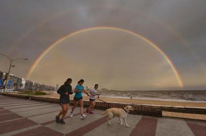 (FILES) In this file picture taken on January 13, 2019 women jog with a dog along Pocitos Rambla as a double rainbow appears during sunset over Montevideo, months before the COVID-19 novel coronavirus appeared in China and expanded around the world. - The European Union on June 30, 2020 agreed to open its border to 15 countries from where travellers can reach Europe from July 1. Non-essential travel to the EU has been banned since mid-March due to the COVID-19 novel coronavirus pandemic, but restrictions are to be gradually lifted starting July 1, as the infection rate recedes. Canada, Japan, Australia, New Zealand and Uruguay were included without conditions. (Photo by Mariana SUAREZ / AFP)