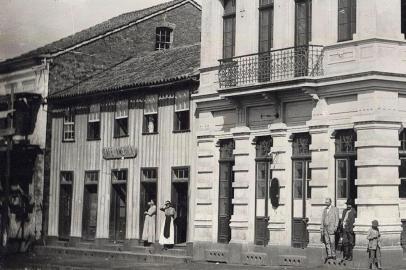 Esquina da Avenida Júlio de Castilhos com a Rua Marquês do Herval por volta de 1915. Era onde se situava o antigo Banco Pelotense (atual Banrisul) e, ao lado dele, pela Júlio, o casarão de madeira onde funcionava o Café América. Imóvel pertencia ao ex-intendente de Caxias Miguel Muratore.<!-- NICAID(14543382) -->