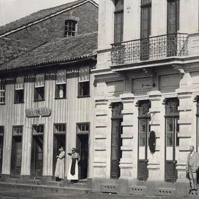 Esquina da Avenida Júlio de Castilhos com a Rua Marquês do Herval por volta de 1915. Era onde se situava o antigo Banco Pelotense (atual Banrisul) e, ao lado dele, pela Júlio, o casarão de madeira onde funcionava o Café América. Imóvel pertencia ao ex-intendente de Caxias Miguel Muratore.<!-- NICAID(14543382) -->