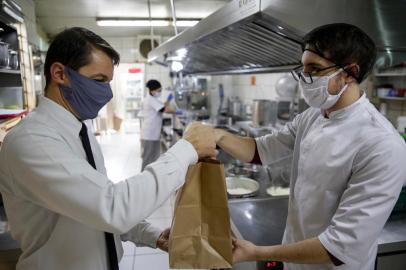 PORTO ALEGRE, RS, BRASIL, 09-07-2020: O chef Matheus Baumbach (D), 25 anos, entrega encomenda para o garçom e agora também entregador Evandro Luis Zanatta, 39. Preparo de refeicoes na cozinha do Restaurante Ratskeller Baumbach, na zona norte. O estabelecimento precisou se adaptar a novas condicoes de trabalho devido a pandemia e agora produz comida apenas para delivery ou take away. A funcao de entregadores foi assumida pelos garcons do restaurante, que levam as encomendas de carro para os clientes. (Foto: Mateus Bruxel / Agencia RBS)Indexador: Mateus Bruxel<!-- NICAID(14541576) -->