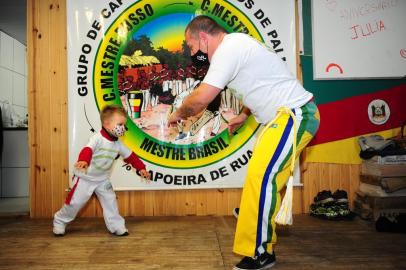  CAXIAS DO SUL, RS, BRASIL, 16/07/2020. Projeto Herdeiros de Palmares ensina capoeira para crianças e adolescentes em vulnerabilidade social no bairro Reolon, em Caxias do Sul. Os voluntários também oferecem refeições para as crianças e suas famílias. Uma vaquinha digital organizada por uma ONG busca recursos para a construção de um refeitório e ampliação da sede, hoje improvisada na casa do criador do projeto. Na foto, Mestre Russo (criador do projeto) com o filho Rafael, 3 anos. (Porthus Junior/Agência RBS)<!-- NICAID(14546417) -->