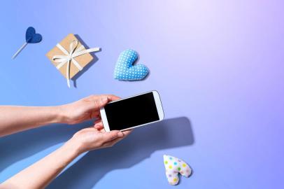 Woman holding her smartphone with small gift and heart cushionsCelular, Smartphone, tecnologia, conectividade. Foto:Tierney / stock.adobe.comFonte: 334229597<!-- NICAID(14554132) -->