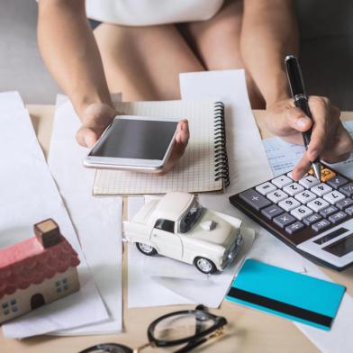 Young woman using smart phone and checking bills, taxes, bank account balance and calculating expenses in the living room at homecontabilidade, escritorio, calculos, calculadora, finanças. Foto: Kittiphan /  stock.adobe.comFonte: 220613223<!-- NICAID(14555710) -->