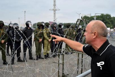  A demonstrator gestures towards law enforcement officers standing guard behind a barbwire fence during a rally of opposition supporters to protest against disputed presidential elections results in Minsk on August 23, 2020. (Photo by Sergei GAPON / AFP)Editoria: WARLocal: MinskIndexador: SERGEI GAPONSecao: electionFonte: AFPFotógrafo: STR<!-- NICAID(14574641) -->