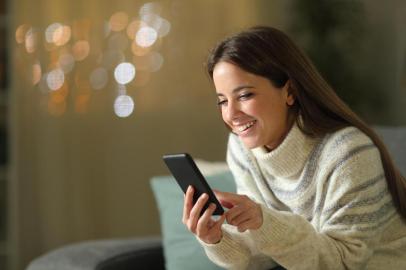  Happy woman in winter using mobile phone in the night sitting on a couch in the living room at homeFonte: 307475303<!-- NICAID(14437256) -->