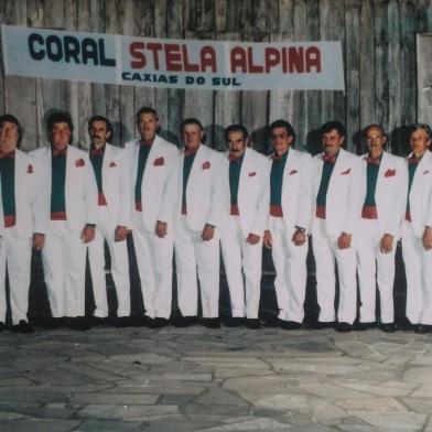 Uma das primeiras formações do grupo, em meados dos anos 1980, ainda com a denominação Coral Stela Alpina. Da esquerda para a direita estão Bortolo Menegol, Angelo Perini, Divino Pissaia, Arnaldo Pastori, Alziro Perini, Luiz Bertoni, Raimundo Sirena, José Demoliner, Armando Bertoni, José Comiotto, João Andreis, Honorino Rossa, Angelo Menegol, Domingos Dal Picol, Ledovino Isotton e Alcides Pissaia. <!-- NICAID(14581408) -->