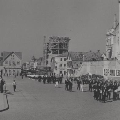 Desfile Cívico da Semana da Pátria. Momento da passagem dos funcionários da Metalúrgica Abramo Eberle & Cia. O local é a Rua Sinimbu, entre as ruas Marquês do Herval e Dr. Montaury, em frente à Praça Dante Alighieri. À direita na imagem, vê-se a Catedral Diocesana, mais ao fundo, a Casa Minghelli e à sua direita, o prédio da Metalúrgica Abramo Eberle em construção. Foto de setembro de 1943<!-- NICAID(10791926) -->