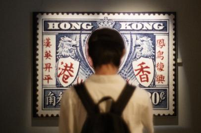 In this photo taken on October 18, 2020 a visitor stands in front of a picture of a stamp during colonial time at The Hong Kong Story exhibition on its last day of opening before a two-year revamp, at the Hong Kong History Museum in Hong Kong. (Photo by Yan ZHAO / AFP)<!-- NICAID(14620038) -->