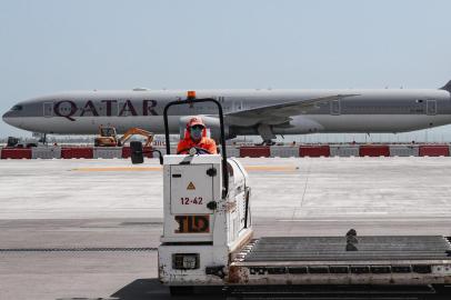 (FILES) In this file photo taken on April 1, 2020, an airport worker wearing a face mask (protective measure during the COVID-19 coronavirus pandemic) mans a luggage trolley while behind him is seen a Qatar Airways Boeing 777 aircraft at Hamad International Airport in the Qatari capital Doha. - Revelations that passengers flying through Doha were forced to endure vaginal inspections have upended Qatars efforts to boost its reputation before the Gulf state hosts World Cup 2022, experts say. Officers marched women off a Sydney-bound Qatar Airways flight earlier this month and forced them to undergo intimate examinations after a newborn baby was found abandoned in an airport bathroom. (Photo by KARIM JAAFAR / AFP)<!-- NICAID(14626881) -->