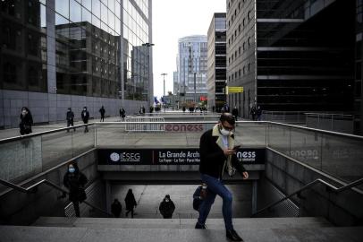 People wearing protective face masks walk by high-rise buildings during the morning rush hour as they arrive at the business district of La Defense west of Paris on October 16, 2020 as the country faces a new wave of infections to the Covid-19 (the novel coronavirus). - La Defense, the largest European business district and the fourth largest in the world, had to reshape its activity following the Covid-19 pandemic: work from home, barrier measures and safety guidelines. According to Paris-La Defense association district, 60% of its workers have returned to the office. However, following the lockdown, the generalisation of home working, the partial closure of bars and restaurants and, now, the curfew, the daily life of some 500 companies and 180,000 employees is permanently affected. (Photo by Christophe ARCHAMBAULT / AFP)<!-- NICAID(14628652) -->