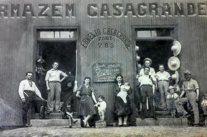 Armazém Casagrande, na Avenida Rio Branco, em 1942. De pé, da esquerda para a direita, Otávio Onzi, Ernesto Casagrande, Adélia Muner Casagrande (esposa de Ernesto), com as filhas Irondina Casagrande Mocelin (sentada) e Ivone Casagrande Milan (em cima da pedra), Dulce Muner (com a filha Renata no colo), Otávio Casagrande (irmão de Ernesto), Alexandre Dossin (atrás do chapéu), Armando Paniz (filho de Zeferino) e pessoas das famílias Rech e Barcarolo.<!-- NICAID(14630032) -->