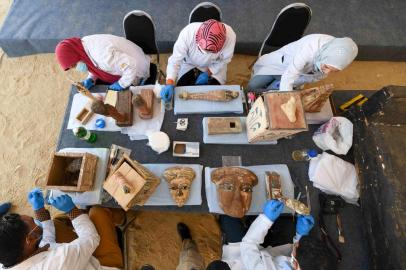 Archaeologists clean statues and funerary masks during the unveiling of an ancient treasure trove of more than a 100 intact sarcophagi, at the Saqqara necropolis 30 kms south of the Egyptian capital Cairo, on November 14, 2020. - Egypt announced the discovery of an ancient treasure trove of more than a 100 intact sarcophagi, the largest such find this year. The sealed wooden coffins, unveiled on site amid fanfare, belonged to top officials of the Late Period and the Ptolemaic period of ancient Egypt. They were found in three burial shafts at depths of 12 metres (40 feet) in the sweeping Saqqara necropolis south of Cairo. (Photo by Ahmed HASAN / AFP)<!-- NICAID(14642913) -->