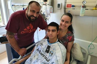  Kevin Scheibler, 18 anos, recebeu na terça-feira um presente e tanto. Duplo. O guri de 18 anos ganhou alta no Moinhos de Vento depois de 25 dias internado. Saiu de lá com uma camiseta do Grêmio enviada pelo volante Darlan e autografada por todos os jogadores do grupo. Kevin sofre de epilepsia mioclônica progressiva, uma doença genética rara, de difícil tratamento, também conhecida como Lafora. Ele precisou ser internado para ajustes na medicação e também em função de uma pneumonia. Os primeiros sintomas surgiram há dois anos. Desde lá, ele  precisa ser hospitalizado com frequência, em função das complicações. Devido às restrições de circulação por causa da pandemia, Darlan não pôde visitar o novo amigo. Mas mandou uma mensagem por vídeo. A entrega da camiseta obedeceu as normas de distanciamento e foi feita aos pais de Kevin, na parte externa do hospital. A ação foi realizada pela ONG Desejo Azul, em parceria com o Moinhos de Vento. O presente enviado pelo ídolo bateu forte no coração da família, que mora em Sapucaia do Sul, e de quem acompanha de perto essa luta. Hoje, em virtude da Lafora, Kevin não anda nem fala e precisa se alimentar por sondas. Os pais, Daniela e André, empresários e fecharam seus negócios para cuidar do filho.Segundo a família, estão em andamento estudo e testes de um novo medicamento nos Estados Unidos e na Espanha. Kevin está na lista para testar o tratamento. Para quem quiser ajudar Kevin, a família criou uma conta no Facebook. Acesse lá em facebook.com/todospelokeke e veja como auxiliar.<!-- NICAID(14664510) -->