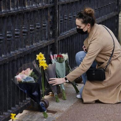 A woman lays a bunch of flowers at the gates of Buckingham Palace in central London on April 9, 2021 after the announcement of the death of Britains Prince Philip, Duke of Edinburgh. - Queen Elizabeth IIs husband Prince Philip, who recently spent more than a month in hospital and underwent a heart procedure, died on April 9, 2021, Buckingham Palace announced. He was 99. (Photo by Tolga Akmen / AFP)<!-- NICAID(14753914) -->