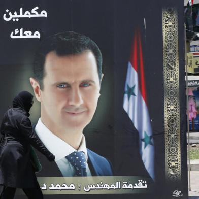 A woman walks past an election campaign billboard depicting Syrian President Bashar al-Assad, a candidate for the upcoming presidential vote, in the capital Damascus, on May 24, 2021. - The Syrian President Bashar al-Assad, whose family has ruled the country for over half a century, faces an election on May 26 meant to cement his image as the only hope for recovery in the war-battered country, analysts say. In the ballot, two challengers will run against him, approved by an Assad-appointed constitutional court, out of a total of 51 applicants. (Photo by LOUAI BESHARA / AFP)<!-- NICAID(14792453) -->