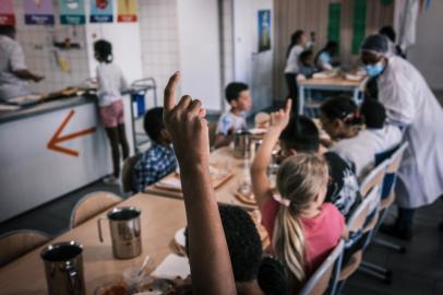 Pupils raise their hands as they have their lunch at the school canteen of the Johannes Masset school in Lyon on May 28, 2021. - Lyons city council, runs by the French ecologist party Europe Ecologie Les Verts (EELV), stated in 2020 the objective to serve 100% organic food to students at the schools canteens. (Photo by JEAN-PHILIPPE KSIAZEK / AFP)<!-- NICAID(14824099) -->