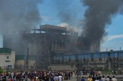 Onlookers watch as smoke bellows from a massive fire that broke out a day before in a beverage and food factory in Rupganj in the district Narayanganj on July 9, 2021 that has reportedly claimed 43 lives so far. (Photo by Munir Uz zaman / AFP)<!-- NICAID(14829710) -->