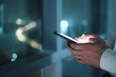 Hands Of Business Man Typing Text Message On PhoneMan working in modern office late at night. Busy caucasian manager at work texting on cell phone, with city and traffic lights in background. Close-up of hands holding smartphoneFonte: 243193396<!-- NICAID(14839125) -->