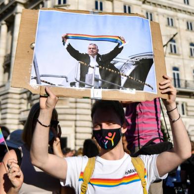 (FILES) In this file photo taken on June 14, 2021 a participant holds a placard showing Hungarian Prime Minister Viktor Orban holding a scarf in rainbow colours, in front of the parliament building in Budapest, during a demonstration against the Hungarian governments draft bill seeking to ban the promotion of homosexuality and sex changes. - Hungarys Prime Minister Viktor Orban said on July 21, 2021 that a referendum would be held to gauge domestic support for a controversial LGBTQ law, after the European Commission launched legal action against Budapest over the measure. (Photo by GERGELY BESENYEI / AFP)<!-- NICAID(14840710) -->