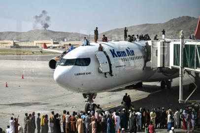 Afghan people climb atop a plane as they wait at the Kabul airport in Kabul on August 16, 2021, after a stunningly swift end to Afghanistans 20-year war, as thousands of people mobbed the citys airport trying to flee the groups feared hardline brand of Islamist rule. (Photo by Wakil Kohsar / AFP)<!-- NICAID(14863716) -->