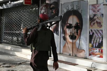 (FILES) In this file photo taken on August 18, 2021, a Taliban fighter walks past a beauty salon with images of women defaced using spray paint in Shar-e-Naw in Kabul. - US President Joe Biden said in an interview that aired August 19, 2021, that war is not the answer to growing fears for the human rights of women in Afghanistan after the Taliban takeover. The idea that were able to deal with the rights of women around the world by military force is not rational, Biden said in the ABC News interview, his first since the Taliban victory triggered a frantic final US withdrawal. (Photo by Wakil KOHSAR / AFP)<!-- NICAID(14866418) -->