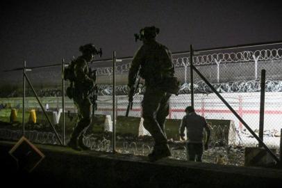 In this picture taken in the late hours on August 22, 2021 British and Canadian soldiers stand guard near a canal as Afghans wait outside the foreign military-controlled part of the airport in Kabul on August 23, 2021, hoping to flee the country following the Talibans military takeover of Afghanistan. (Photo by WAKIL KOHSAR / AFP)<!-- NICAID(14869547) -->