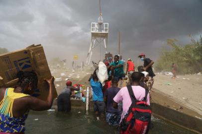 Migrants, many from Haiti, assist each other as they cross the Rio Grande with supplies near the Del Rio-Acuna Port of Entry in Del Rio, Texas, on September 18, 2021. - The United States said on September 18 that it would ramp up deportation flights for thousands of migrants who flooded into the Texas border city of Del Rio, as authorities scramble to alleviate a burgeoning crisis for President Joe Bidens administration. The migrants who poured into the city, many of them Haitian, were being held in an area controlled by US Customs and Border Protection (CBP) beneath the Del Rio International Bridge, which carries traffic across the Rio Grande river into Mexico. (Photo by PAUL RATJE / AFP)<!-- NICAID(14895828) -->