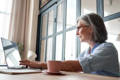 Smiling mature middle aged woman using laptop computer sitting at workplace.Smiling professional mature middle aged business woman using laptop computer sitting at workplace desk. Happy senior old lady 60s grey-haired businesswoman executive working on pc at home from office.Fonte: 383390479<!-- NICAID(14915278) -->