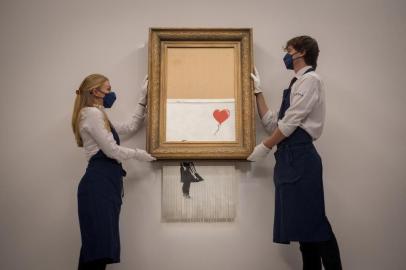 (FILES) In this file photo taken on September 3, 2021 assistants pose alongside an artwork titled Love is the Bin by British street artist Banksy during a photocall at Sothebys auction house in central London. - A partially shredded canvas of one of British artist Banksys most celebrated works is expected to sell for millions when it goes under the hammer on October 14. (Photo by Tolga Akmen / AFP) / RESTRICTED TO EDITORIAL USE - MANDATORY MENTION OF THE ARTIST UPON PUBLICATION - TO ILLUSTRATE THE EVENT AS SPECIFIED IN THE CAPTIONEditoria: ACELocal: LondonIndexador: TOLGA AKMENSecao: culture (general)Fonte: AFPFotógrafo: STR<!-- NICAID(14915417) -->