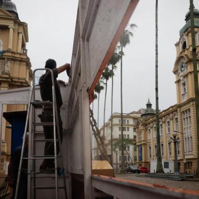 Equipes trabalham na montagem da 67ª edição da Feira do LivroNa tarde deste sábado (23), pelo menos 15 das 56 bancas da Feira do Livro desde ano já haviam sido montadas na Praça da Alfândega, no centro de Porto Alegre. Além de montar os espaços, a equipe também trabalha para levantar a estrutura da cobertura, que irá proteger o público em dias de chuva. O trabalho começou na última semana e deve ser concluído na próxima quarta-feira (27), quando os livreiros poderão começar a ocupar os locais. Em formato híbrido, a 67ª edição do evento começará na sexta-feira (29) e segue até o dia 15 de novembro.<!-- NICAID(14923210) -->