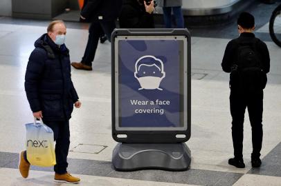 Pedestres circulam pela estação de trem da Rua Liverpool, em Londres, onde placa alerta para a necessidade de usar máscara para evitar a transmissão da covid-19Pedestrians, some wearing face coverings to combat the spread of Covid-19, walk past a sign asking commuters to Wear a face covering, at Liverpool Street train station in central London on December 18, 2021. - London mayor Sadiq Khan on Saturday declared a major incident in the British capital due to the spread of the Omicron variant. More than 65,000 new cases were confirmed in London over the past seven days, and 26,418 cases reported in the last 24 hours -– the highest number since the start of the pandemic. (Photo by Tolga Akmen / AFP)<!-- NICAID(14971879) -->