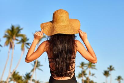 Woman in sunhat on a beachUma mulher com um chapéu de sol de pé sobre um céu azul. Foto: kobeza / stock.adobe.comIndexador: Dmitry KobezaFonte: 109338007<!-- NICAID(14975474) -->