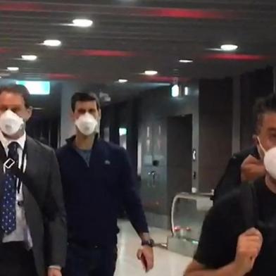 This screen grab taken from AFPTV shows Serbias Novak Djokovic (2nd L) preparing to depart from Melbourne Airport in Melbourne on January 16, 2022, after losing a sensational legal battle over his coronavirus vaccination status with his dream of clinching a record 21st Grand Slam in tatters. (Photo by Mell CHUN / AFP) / -- IMAGE RESTRICTED TO EDITORIAL USE - STRICTLY NO COMMERCIAL USE --Editoria: SPOLocal: MelbourneIndexador: MELL CHUNSecao: tennisFonte: AFPFotógrafo: STR<!-- NICAID(14991153) -->