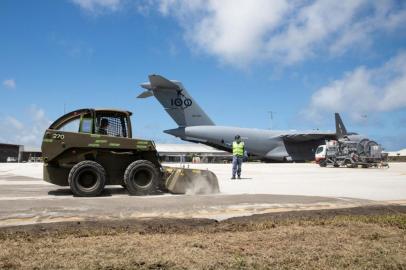 This handout photo taken and released on January 20, 2022 by the Royal Australian Air Force and the Australian Defence Force shows Sergeant Antony Ahchow (C) from No. 23 Squadron guiding a skid steer loader to sweep volcanic ash off the handstand at Fuaamotu International Airport in Tonga following the January 15 eruption of the Hunga Tonga-Hunga Haapai underwater volcano nearby. (Photo by LACW Emma Schwenke / Australian Defence Force / AFP) / -----EDITORS NOTE --- RESTRICTED TO EDITORIAL USE - MANDATORY CREDIT AFP PHOTO / Australian Defence Force - NO MARKETING - NO ADVERTISING CAMPAIGNS - DISTRIBUTED AS A SERVICE TO CLIENTS<!-- NICAID(14994449) -->