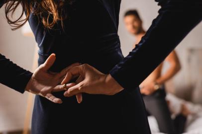 Selective focus of woman with hands behind back taking off wedding ring near shirtless man in bedroomFonte: 372938179<!-- NICAID(15000326) -->