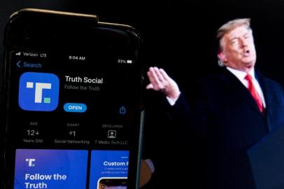 This photo illustration shows an image of former President Donald Trump next to a phone screen that is displaying the Truth Social app, in Washington, DC, on February 21, 2022. - Donald Trumps new social media app started a gradual rollout late February 21st and should be fully operational by late March, potentially raising the former presidents profile more than a year after he was banned by major platforms. Trump has described Truth Social as an alternative to Facebook, Twitter and YouTube, all of which banned him following the assault on the US Capitol by his supporters on January 6, 2021. The former president has been accused of inciting his followers to use force in a bid to overturn the result of the 2020 election. (Photo by Stefani Reynolds / AFP)<!-- NICAID(15022670) -->