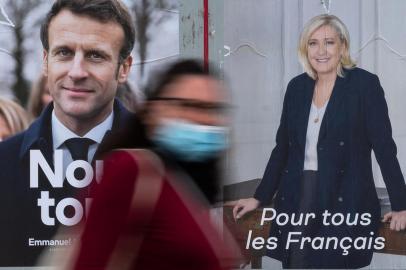 A woman passes by electoral campaign posters of French President and La Republique en Marche (LREM) party candidate for re-election Emmanuel Macron (L) and French far-right party Rassemblement National (RN) presidential candidate Marine Le Pen in Savenay, western France on April 19, 2022. - Emmanuel Macron won 27.85 percent of votes in the first round of Frances presidential election, while far-right veteran Marine Le Pen scored 23.15 percent, according to final results from the interior ministry on April 18, 2022. (Photo by Loic VENANCE / AFP)<!-- NICAID(15072338) -->