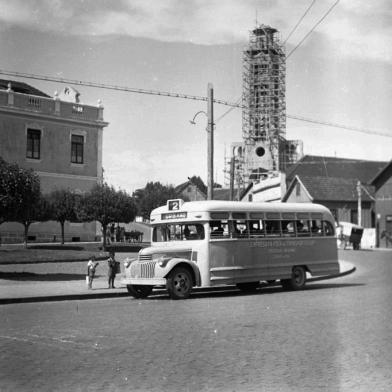 Trecho da Avenida Júlio de Castilhos no enntroncamento com a Feijó Júnior, no bairro São Pelegrino, por volta de 1950. No local vê-se a Praça João Pessoa, a antiga sede do Colégio São Carlos e a Igreja de São Pelegrino sendo construída. À direita, meio cortada, a casa do morador e dentista Aparício Postali. <!-- NICAID(14026004) -->