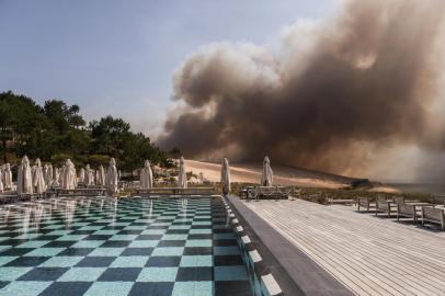 This photograph taken in Pyla sur Mer, on July 18, 2022 shows the smoke rising from the forest fire in La Teste-de-Buch, seen from the 5 stars hotel, La Corniche, in front of the Pilat dune. - In scorching heat, with more than 40°C, some 8,000 people had to leave - in a preventive manner according to the prefecture - the Miquelots and Pyla-sur-Mer, districts of the municipality of La Teste-de-Buch, a town of 28,000 inhabitants where 4,300 hectares of forest went up in smoke. (Photo by THIBAUD MORITZ / AFP)<!-- NICAID(15151778) -->