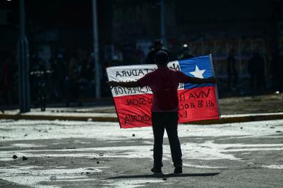 A demonstrator holds a Chilean national flag during clashes with riot police which erupted in a protest on the third anniversary of a social uprising against rising utility prices, in the surroundings of the Baquedano square in Santiago, on October 18, 2022. - The sustained movement forced then president Sebastian Pinera to increase tax spending and expand social programs, resulting in 2021 in the largest increase in public spending in the countrys history at 33 percent. (Photo by MARTIN BERNETTI / AFP)<!-- NICAID(15240292) -->