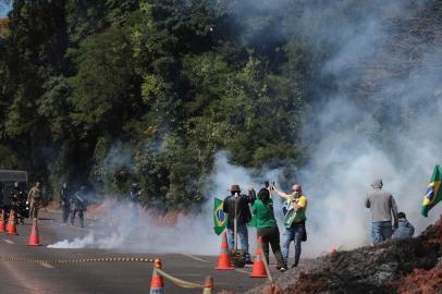 A supporter of President Jair Bolsonaro holds a Brazilian flag and a figure of a virgin as he confronts Military Police shock troops trying to disperse protesters during a blockade on the BR-116 highway in Novo Hamburgo, Rio Grande do Sul State, Brazil, on November 1, 2022. - Supporters of Brazilian President Jair Bolsonaro blocked major highways for a second day as tensions mounted over his silence after narrowly losing re-election to bitter rival Luiz Inacio Lula da Silva. Federal Highway Police (PRF) on Tuesday reported more than 250 total or partial road blockages in at least 23 states by Bolsonaro supporters, while local media said protests outside the countrys main international airport in Sao Paulo delayed passengers and led to several flights being cancelled. (Photo by Silvio AVILA / AFP)<!-- NICAID(15252484) -->