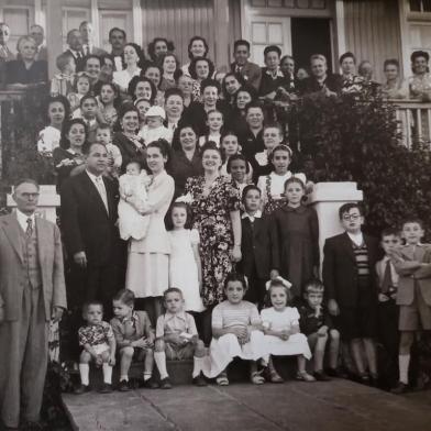 Batizado de Regina Yara Veronese Mascia, filha de Ruy Mascia e Nelly Veronese Mascia, nascida em 11 de fevereiro de 1948. O registro feito pelo Studio Geremia ocorreu defronte ao extinto casarão de madeira localizado na Rua Bento Gonçalves, entre a Alfredo Chaves e a Guia Lopes, onde residia o casal Antonieta Agostinelli Veronese e Luiz Veronese, avós de Regina e pais de dona Nelly.A festa, obviamente, reuniu dezenas de familiares e amigos, boa parte deles eternizada na ¿foto oficial¿. A bebê Regina Yara está junto aos padrinhos Cecy Mascia e Carlos GottschallTambém estão ali, à esquerda, Ruy Mascia (de terno branco), Luiz Veronese (ao lado dele), a esposa Antonieta (mais ao centro), Gessy Agostinelli Divan e o filho José Armando (no colo, de boné branco), o casal Nilza Serafini Veronese e Attilio Veronese, Felice Veronese Casagrande, Honorina Bertier Agostinelli, Hélio Agostinelli, a atriz de novelas de rádio Lucita Fonseca (com o filho Vicente Newton), o casal Henrique Veronese e Clotilde Costi Veronese, Iolanda Maggi, Santiago e Inês Mascia, Gino Focardi, Olga Agostinelli Focardi e Amábile Andreazza Agostinelli.Entre as crianças (à frente, a partir da esquerda) estão José Antônio Veronese Mascia, Marco Aurélio Gottschall, Luiz Santiago Veronese Mascia, Regyna de Queiroz Gazola, Ivan Maggi, Antônio Rath de Queiróz, Juliano Viegas e João Claudio Pante. Mais ao centro vemos ainda Matilde Veronese Saldanha (de laço branco na cabeça, junto aos padrinhos do bebê), Marisa Canalli e Mariazinha de Queiroz Casara.<!-- NICAID(15263162) -->