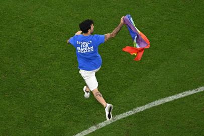 A man invades the pitch holding a LGBT flag as he wears a t-shirt reading Respect for Iranian woman during the Qatar 2022 World Cup Group H football match between Portugal and Uruguay at the Lusail Stadium in Lusail, north of Doha on November 28, 2022. (Photo by MANAN VATSYAYANA / AFP)Editoria: SPOLocal: DohaIndexador: MANAN VATSYAYANASecao: soccerFonte: AFPFotógrafo: STF<!-- NICAID(15279156) -->