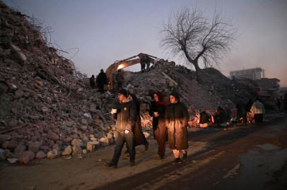 People walk past rubble of collapsed buildings as rescue teams continue to search victims and survivors, after a 7.8 magnitude earthquake struck the border region of Turkey and Syria earlier in the week, in Kahramanmaras on February 12, 2023. (Photo by OZAN KOSE / AFP)<!-- NICAID(15347164) -->